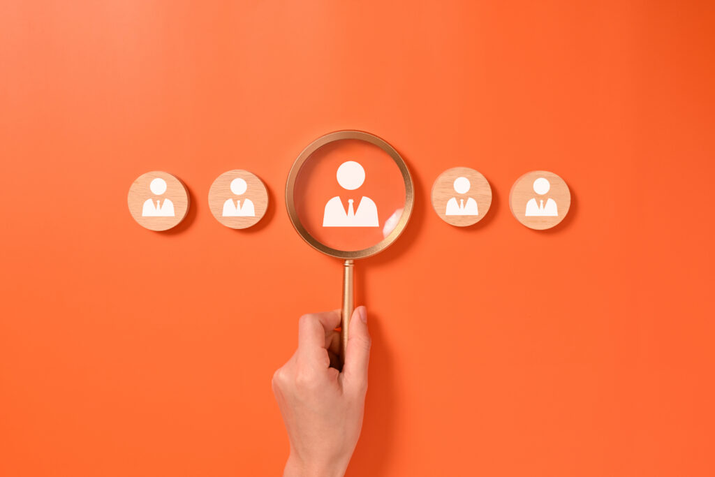 A hand holding a magnifying glass focuses on one customer, illustrating prospecting techniques.